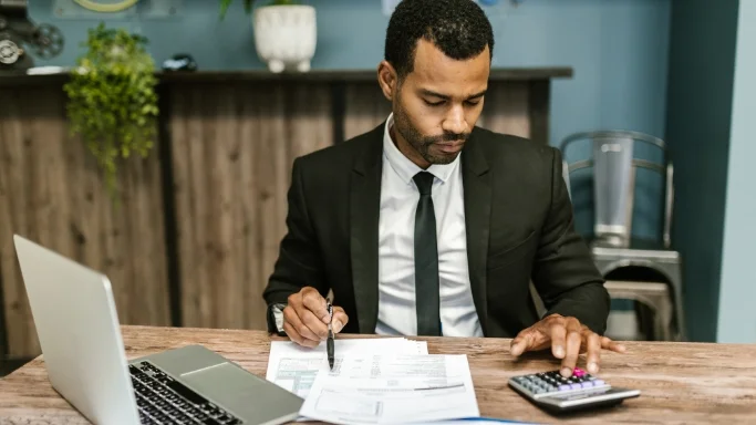 Male accountant analyzing financial documents at his desk and using a calculator.