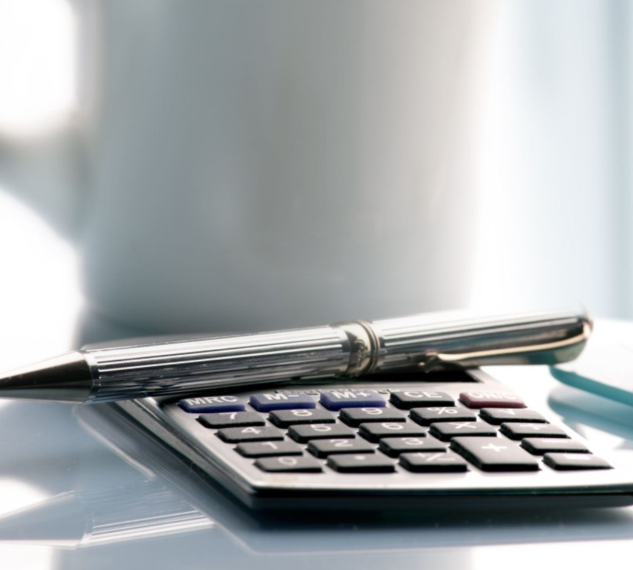 A calculator and pen on a table next to a cup of coffee used for making tax digital (MTD).